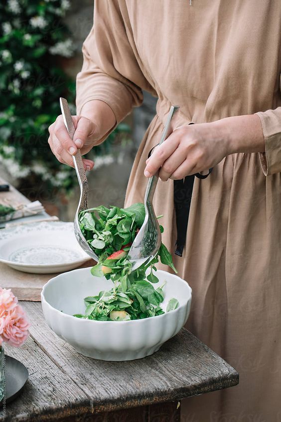 A person seated by a window slowly eating a bowl of grains and vegetables in soft daylight